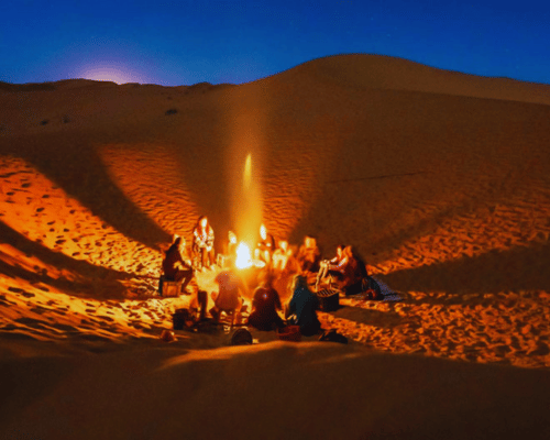 Desert safari Dubai evening campfire experience in the dunes with tourists enjoying a cozy gathering.